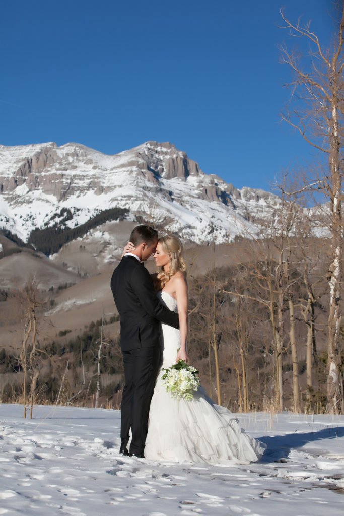 couple hugs with the sneffels range in the back ground of their snowy portrait session.