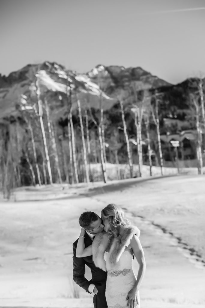 couple kisses with Palmyra Peak in the back ground of their snowy portrait session.