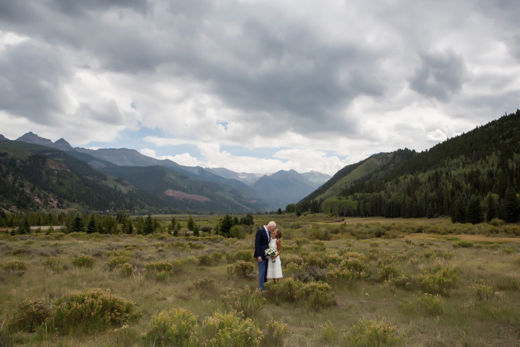 Couple kissing on the valley floor with the mountains and beauty all around them.