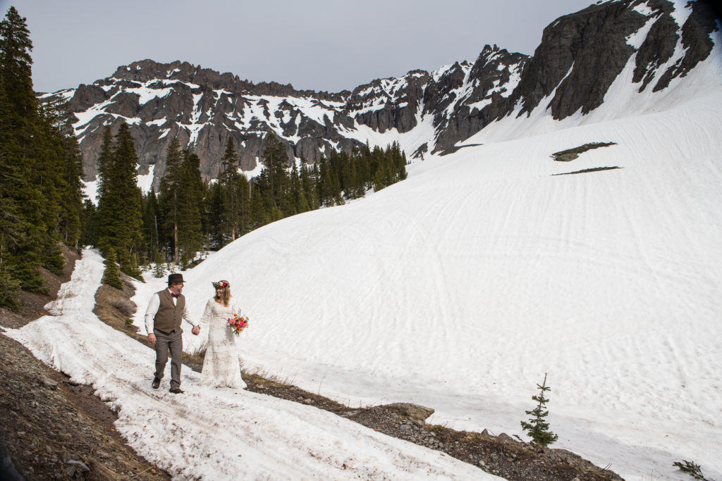 boho bride and groom walk hand in hand with the mountains of the Telluride ski resort in the background. Telluride wedding photographer Real Life Photographs